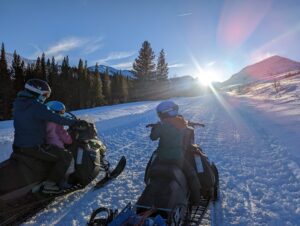 two kids and a woman riding snow bikes