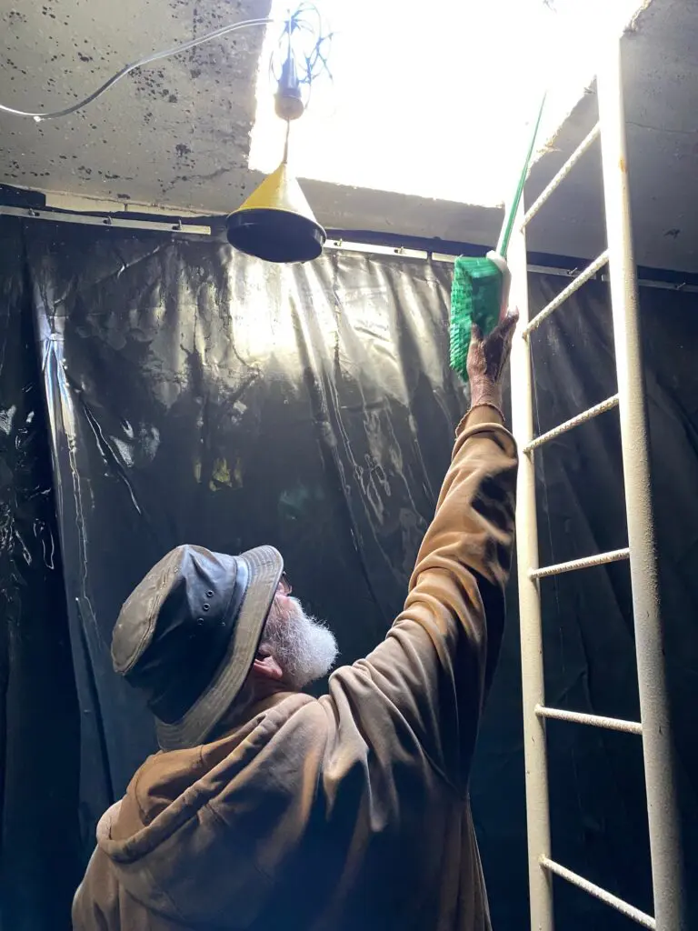 Man handing long handled brush up through ceiling hatch